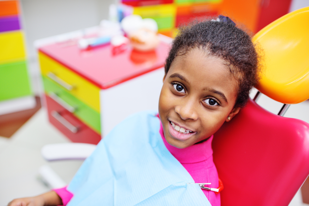 A child sitting in a pediatric dentist’s chair and smiling